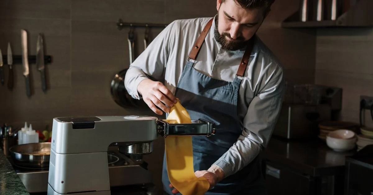 Un chef prépare habilement des pâtes fraîches dans une cuisine professionnelle en utilisant une machine à pâtes.