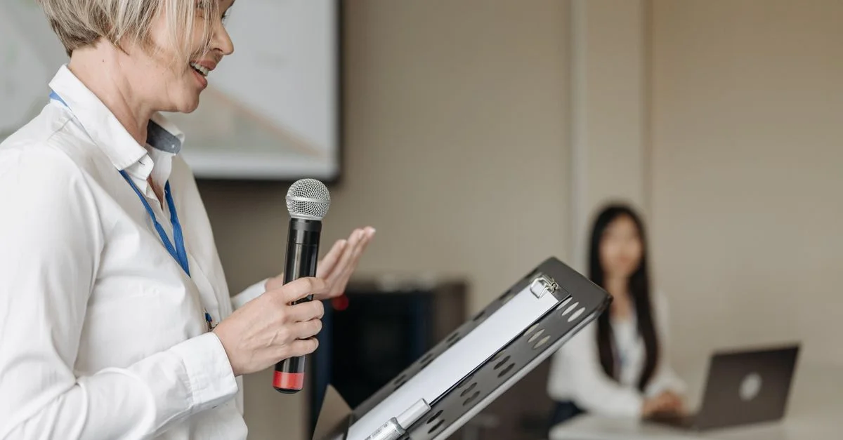 Une femme présentée avec un microphone lors d'un séminaire professionnel avec un membre du public en vue.